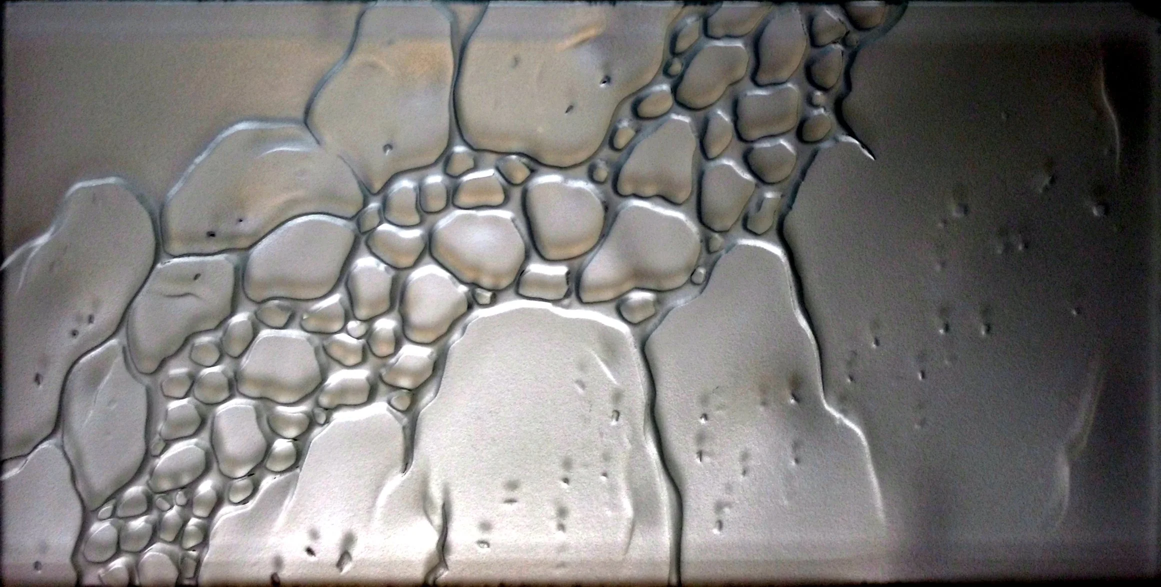 Close-up of unevenly distributed soap bubbles and foam on a metallic surface.