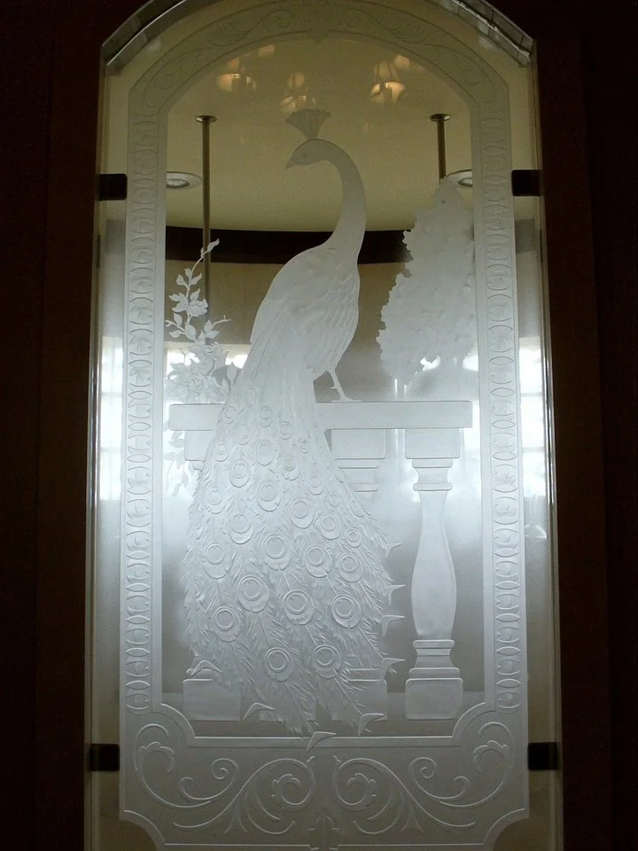 Carved glass panel with a peacock design, featuring the bird with long tail feathers, perched on a banister with decorative foliage and border.