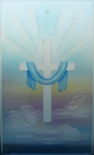 A carved and painted glass with a cross and blue ribbon draped over it, set against a sky background transitioning from yellow to blue, with rays of light and a small star above.