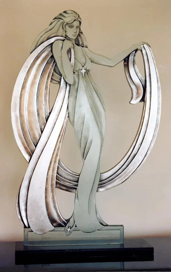 carved glass sculpture with silver leaf flowing wrap on a marble base