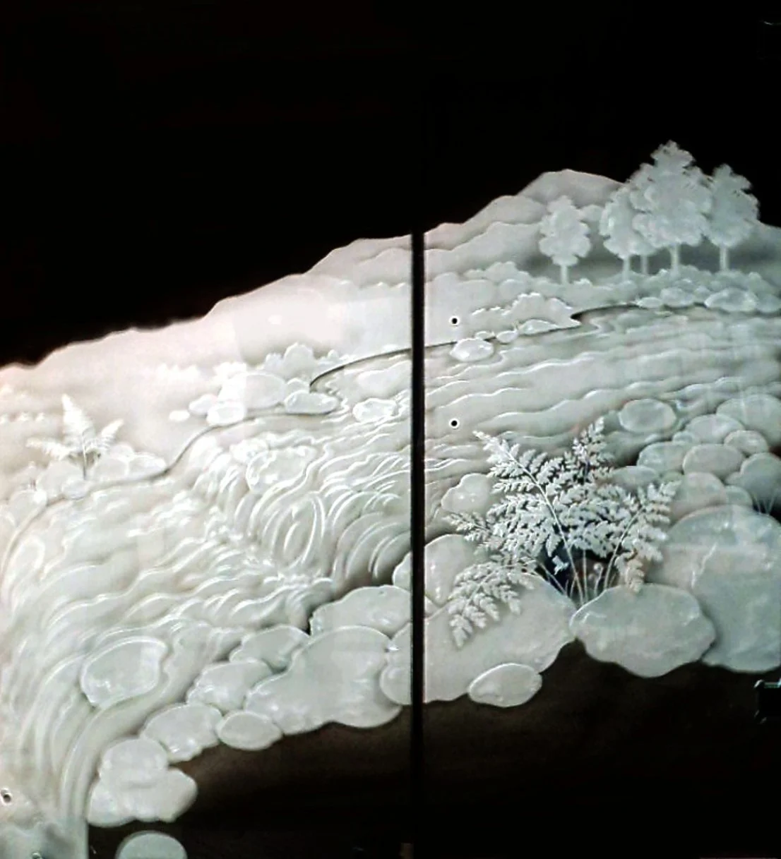 Illuminated carved jade artwork depicting a flowing stream or river with trees and rocks.