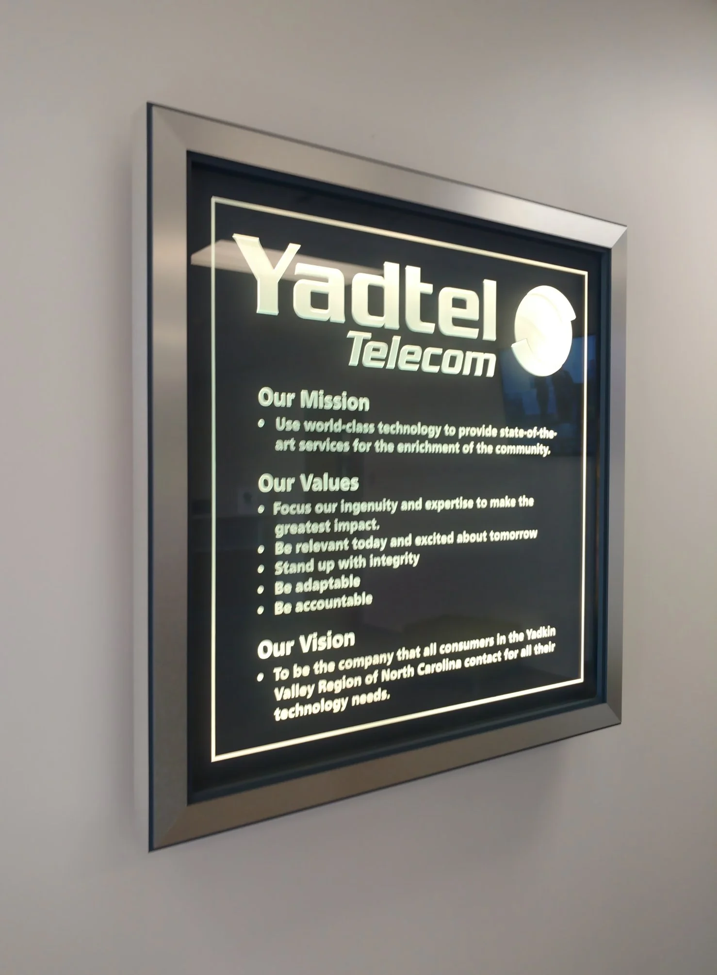 Yadtel Telecom company mission, values, and vision custom glass framed and lit on a wall.