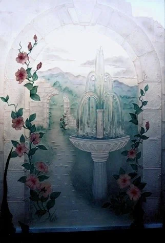 Carved and painted glass installed in bathroom above the tub for privacy. The design is a fountain and stone arch with flowers and scenic landscape.