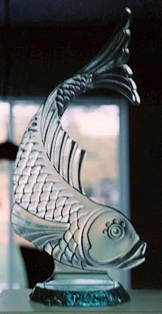 Decorative fish sculpture with a curved tail and detailed scales, placed indoors near a window.