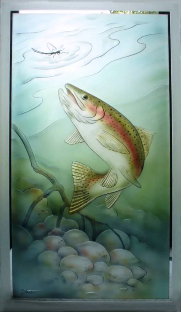 A carved glass painting of a large, colorful trout fish in a stream, with rocks below, and a fly lure above.