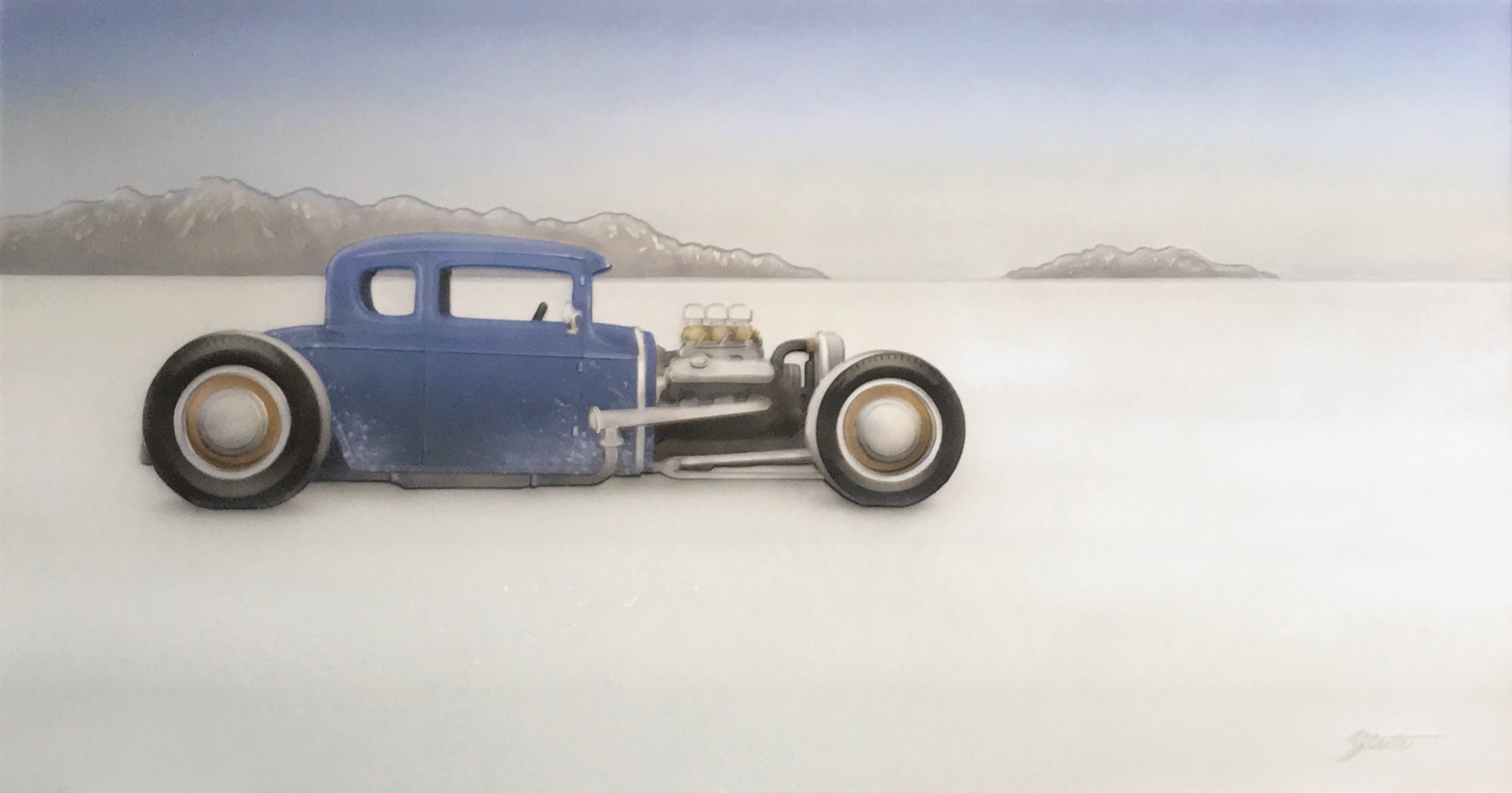 Vintage blue race car with exposed engine on a white surface, mountains in the background.