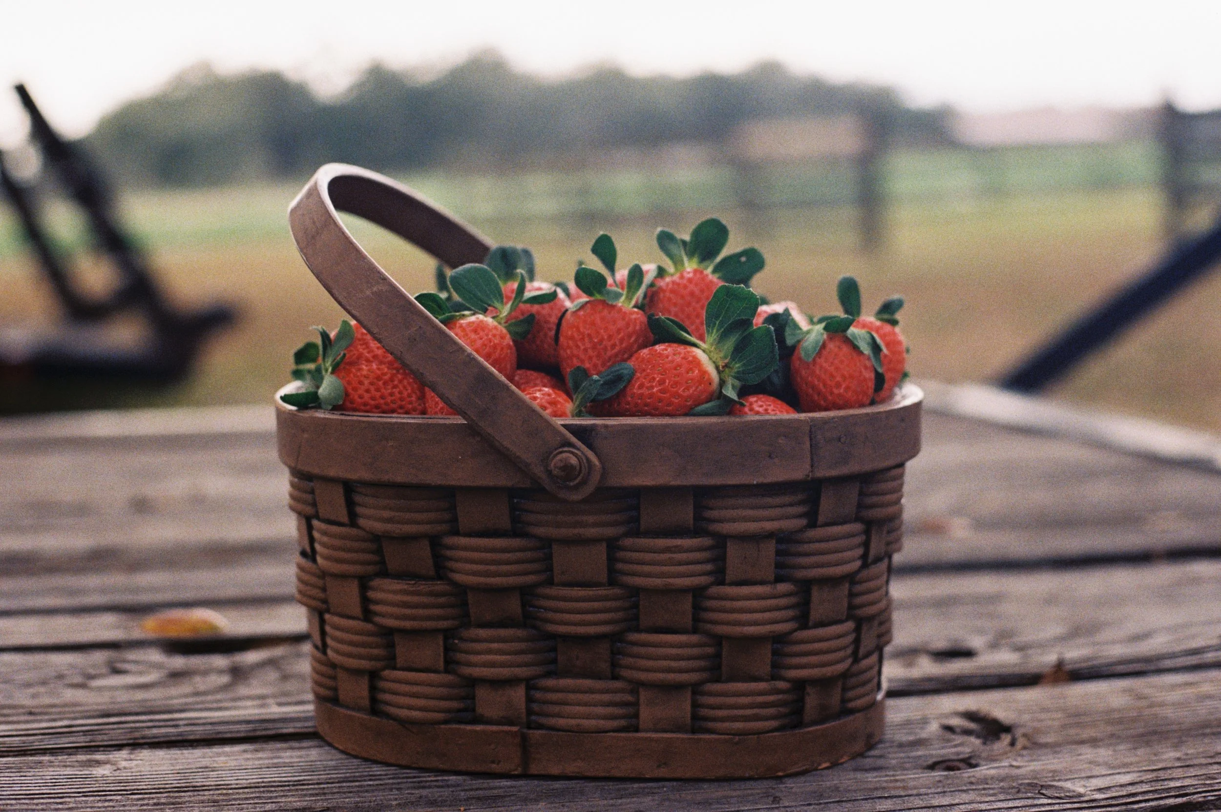 Basket of fresh strawberries on a rustic wooden surface with a blurred outdoor background.