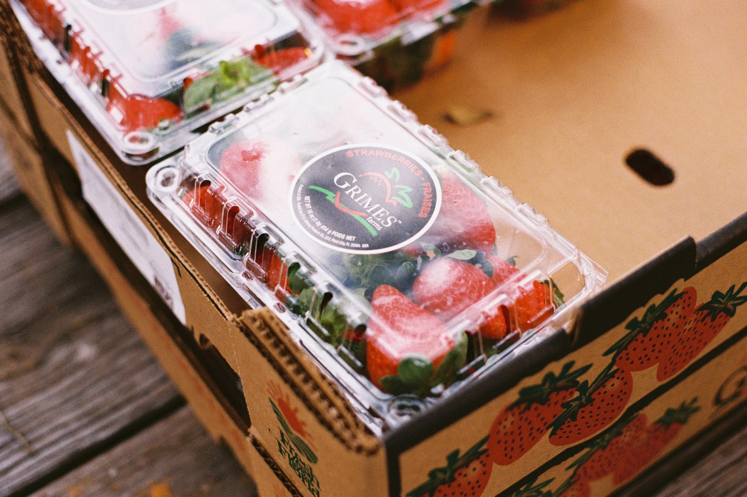 A clear plastic container of strawberries on top of a cardboard box.