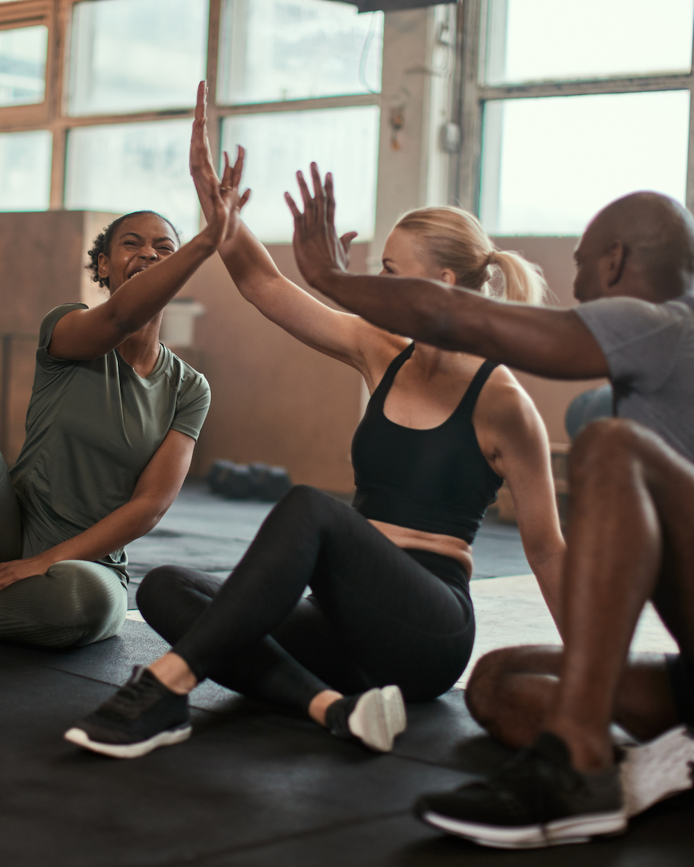 Three people engaging in a high-five during a fitness class in a gym.
