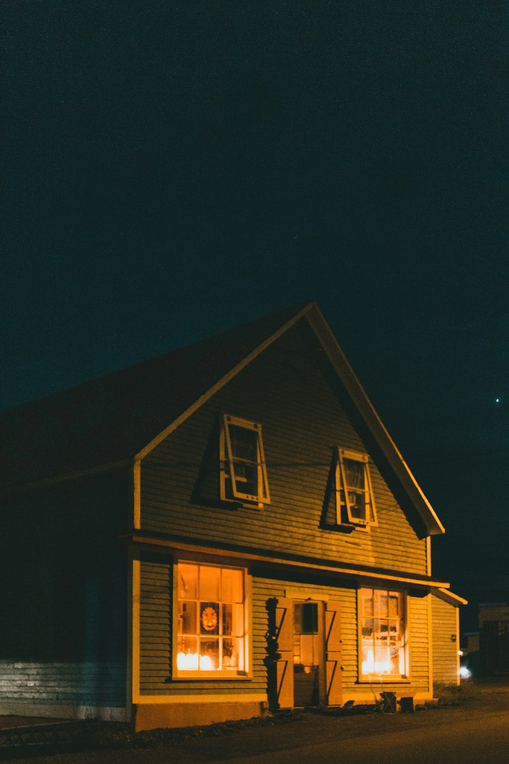 A two-story house with lit candles and decorations visible in the windows at night, with a dark sky and a star.