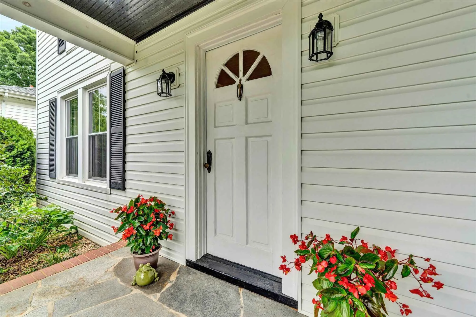 Front porch with white door, black lantern-style lights, and potted plants with red flowers.