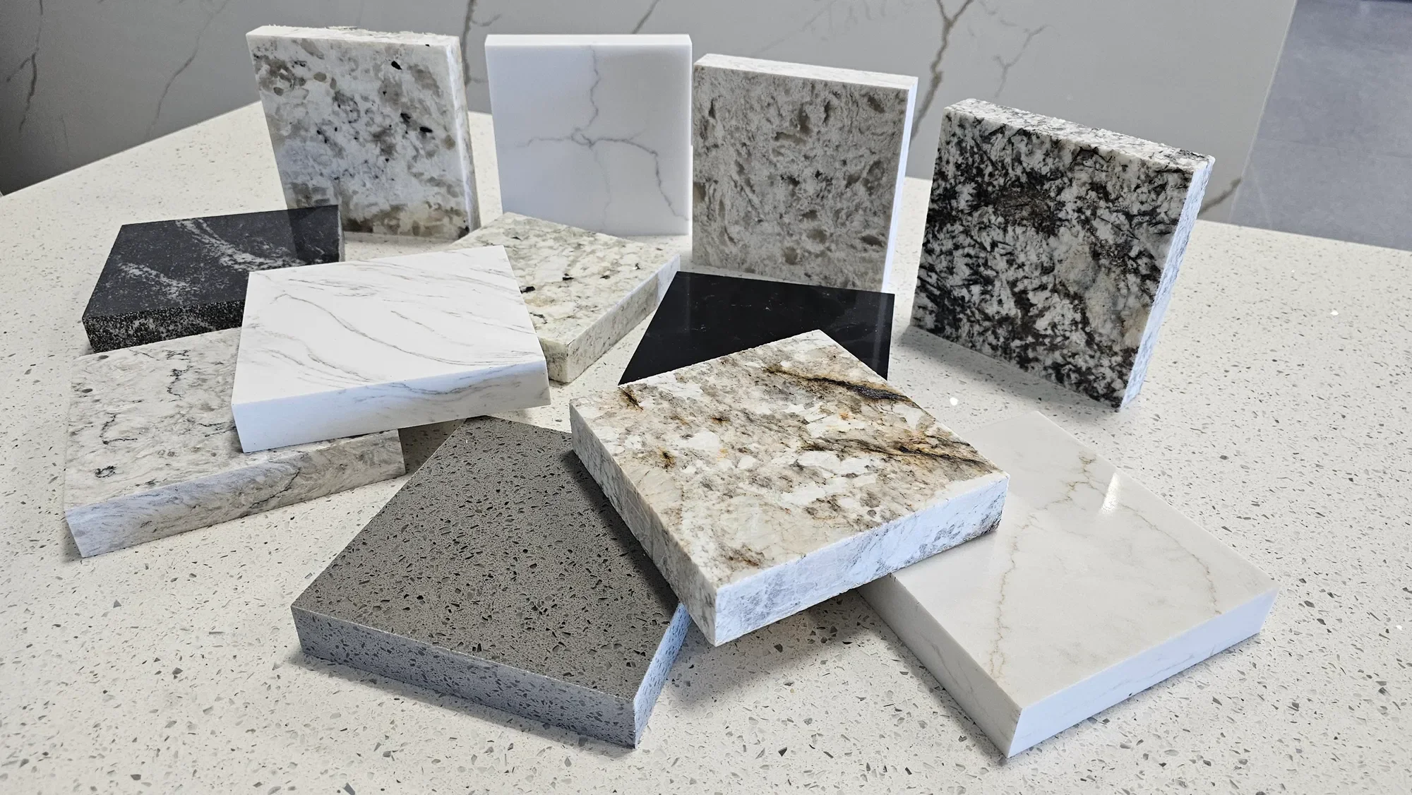 A variety of marble and granite sample tiles arranged on a speckled countertop, showcasing different colors and patterns.
