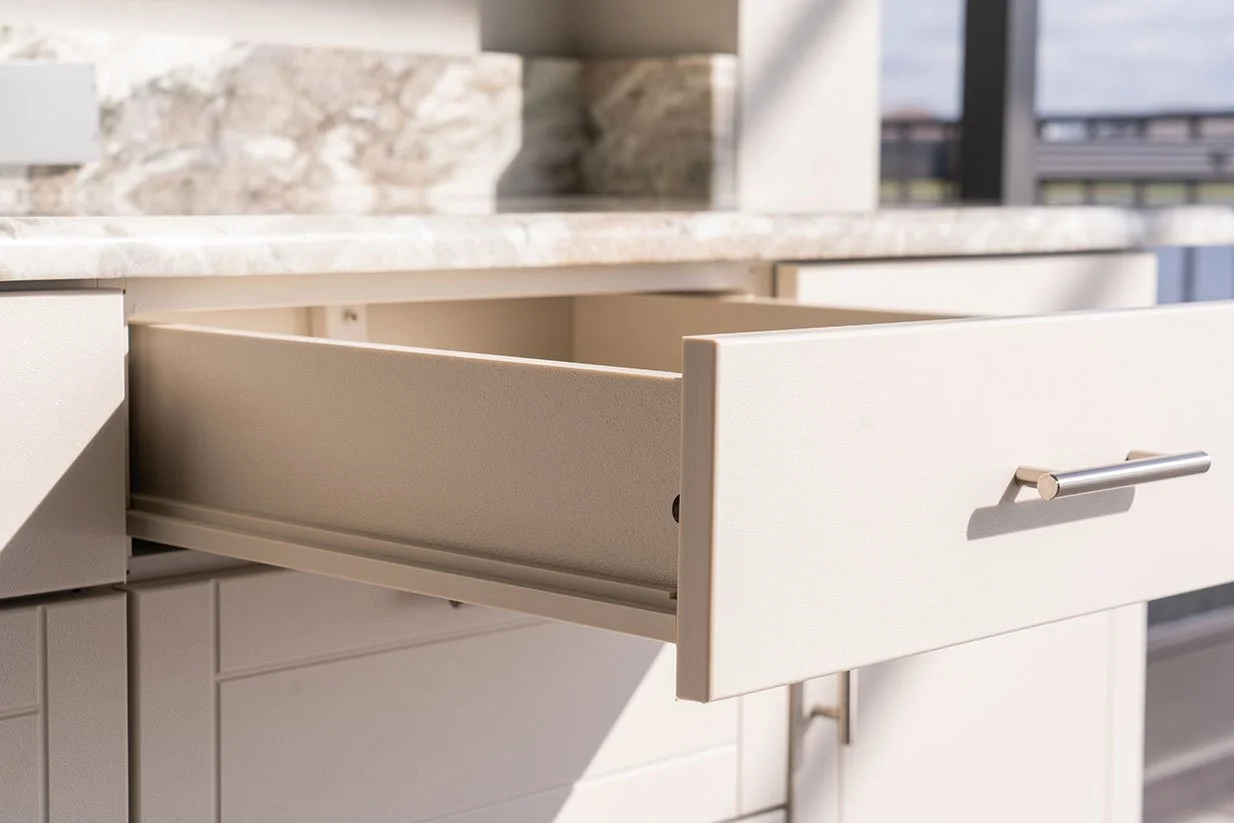 Open kitchen drawer with stainless steel handle, empty and partially extended, in front of marble countertop.
