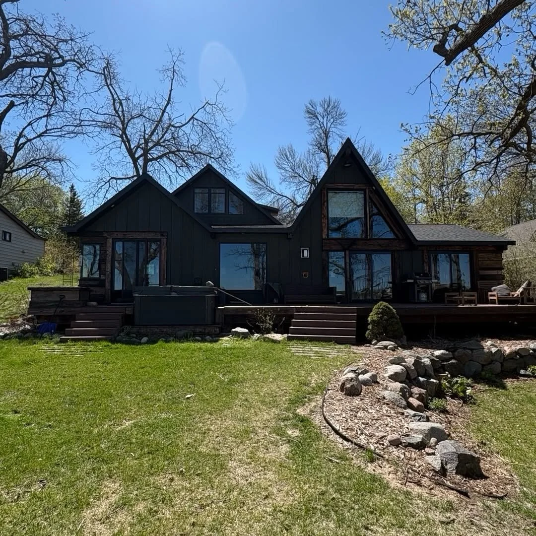 Completed home with tall windows, dark exterior, deck steps, and rock landscaping.