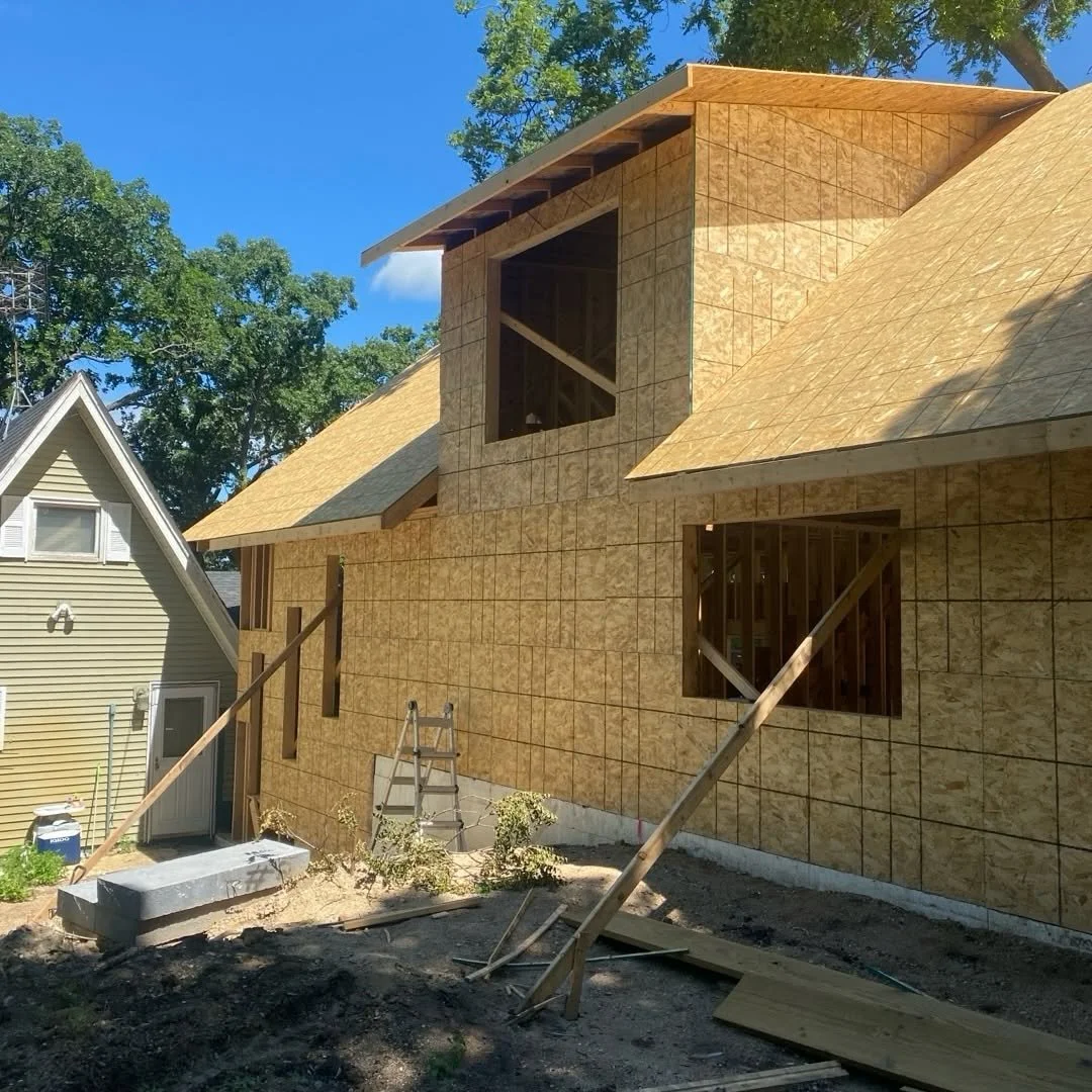 Home exterior during construction with unfinished walls, roof framing, and window openings.