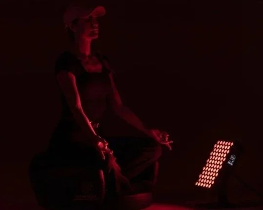 A woman meditating in a dark room illuminated by red light.