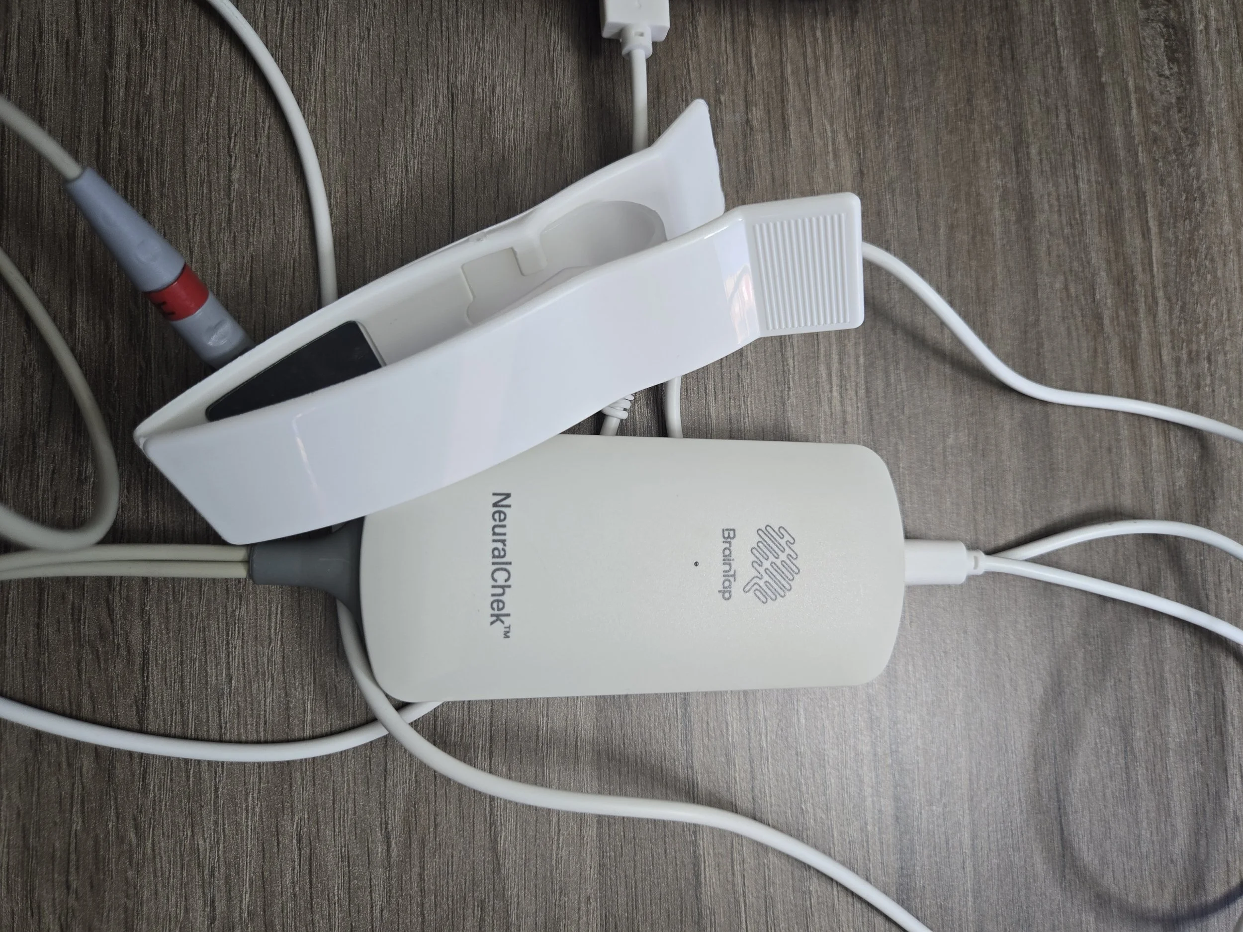 Electronic devices connected with white and gray cables on a wooden surface, including a NeurologicalCheck device and PowerStrip.