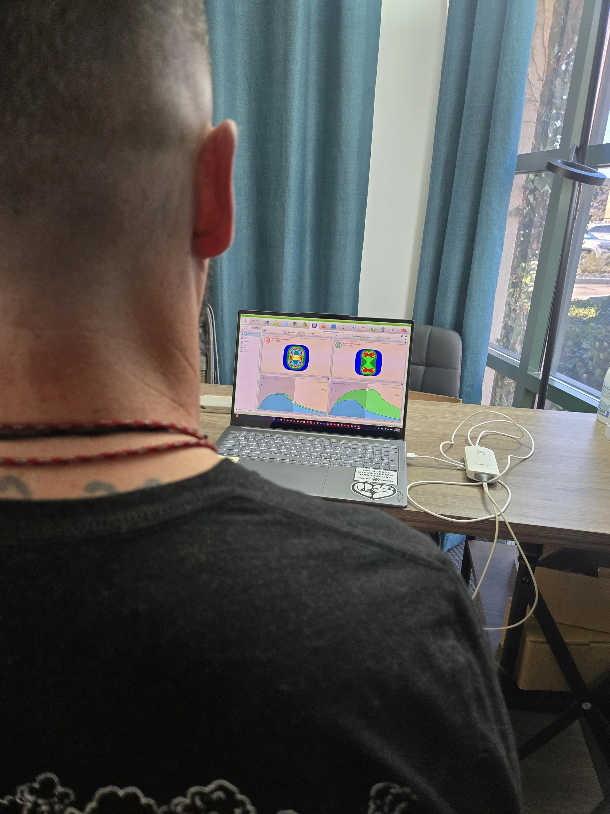 Person with short hair and a tattoo on their neck sitting in front of a laptop displaying color-coded graphs and heatmaps.