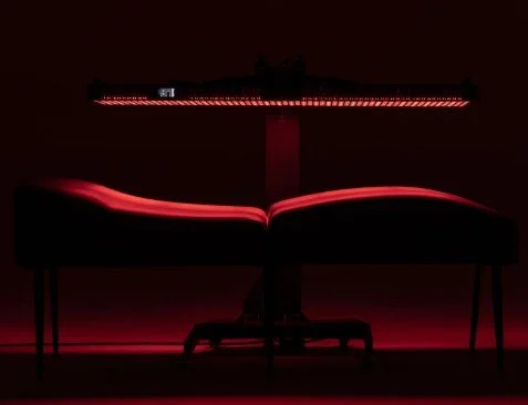 A vibroacoustic bed with a glowing red light overhead, set against a dark background.