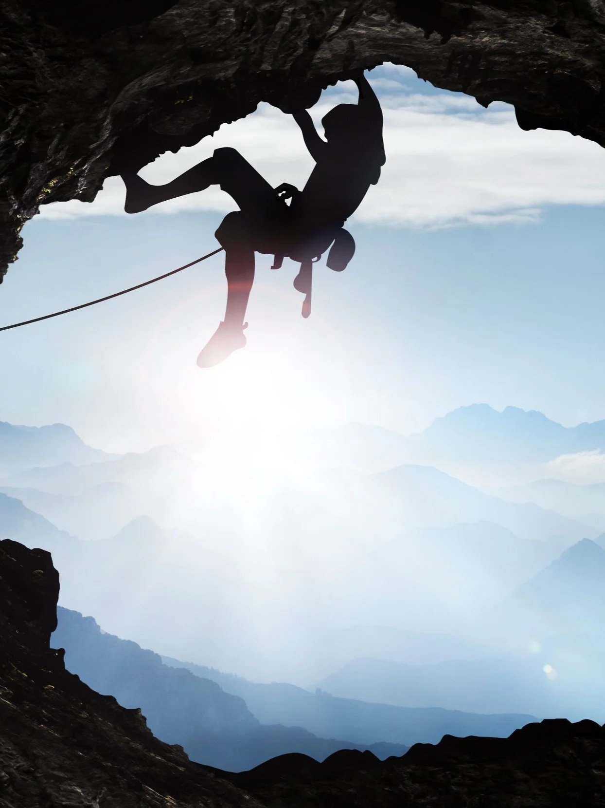 Silhouette of a person rock climbing under a rock arch with mountains in the background.