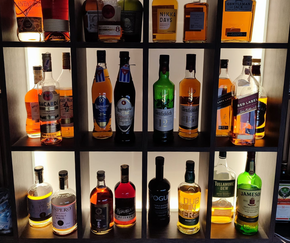 Shelf of various whiskey and liquor bottles in a wooden cabinet with backlighting.