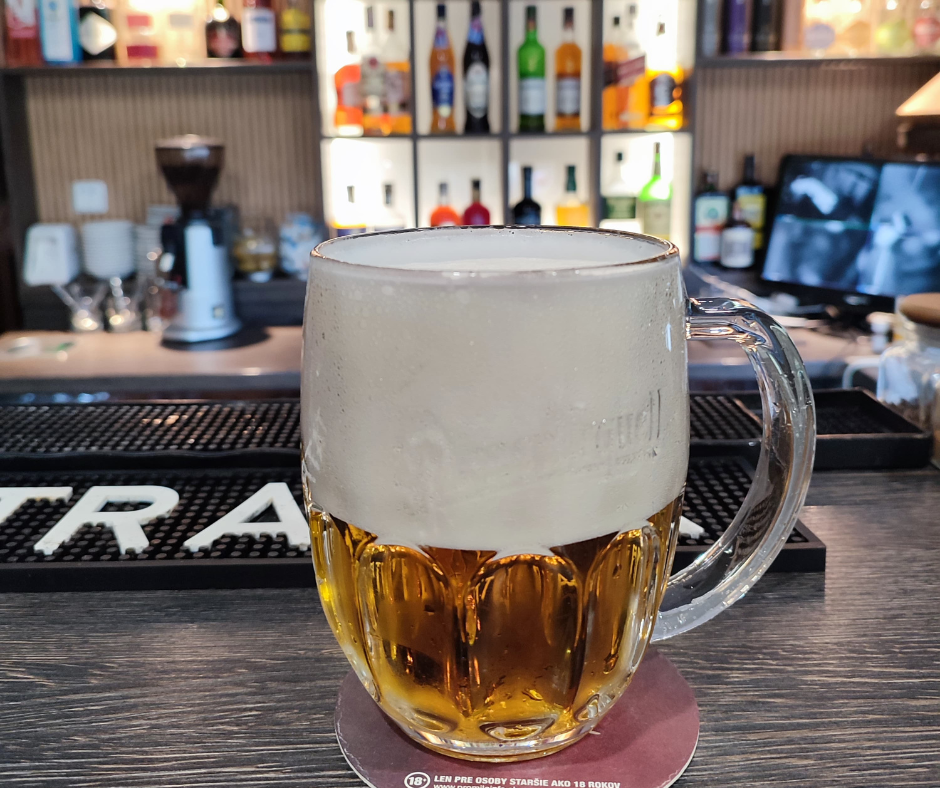 A glass beer mug filled with beer and topped with foam, sitting on a bar counter.