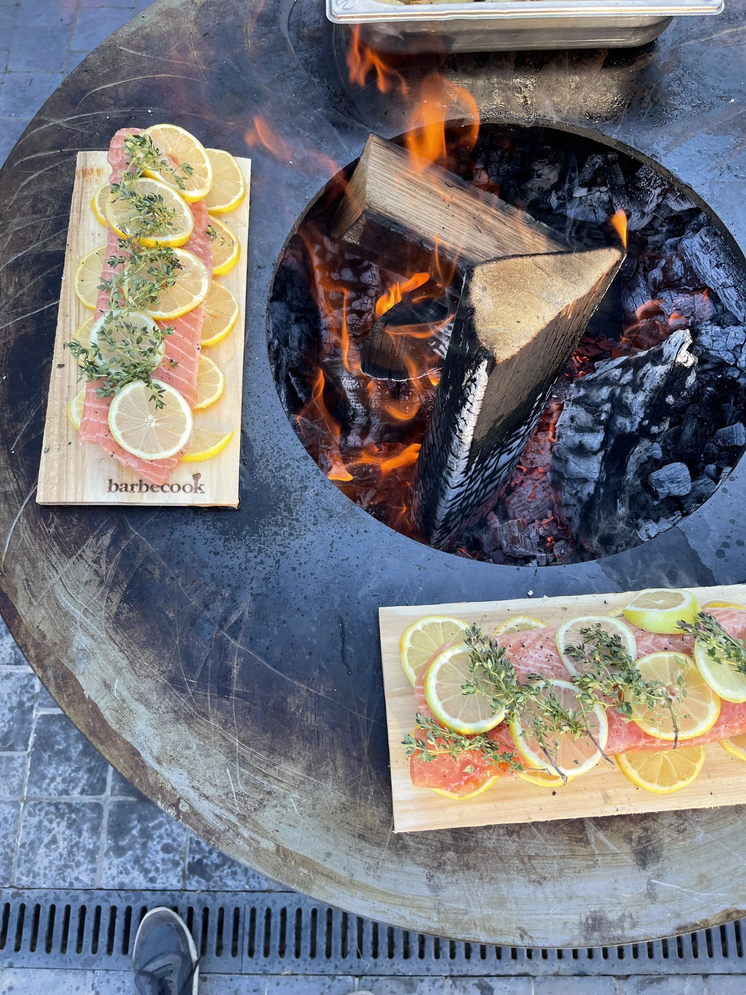 Vissenfilet met citroen en kruiden op houten plank, naast een open vuur onder een grillplaat. #chefvandenberghe , chef van den berghe , private dining, private chef aan huis