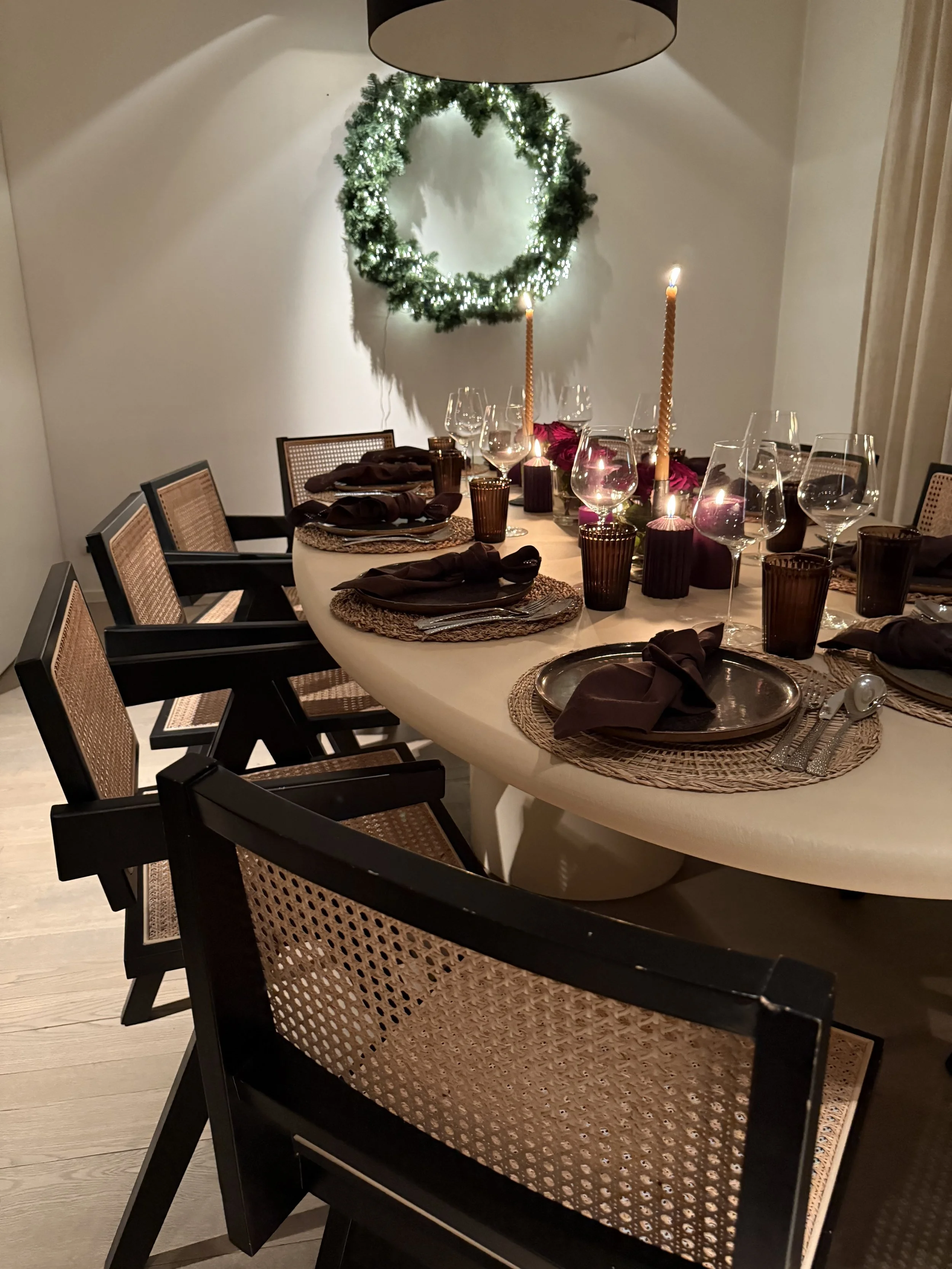 Een feestelijk gedekte eetkamertafel met kaarsen, wijnglazen, en een kerstkrans aan de muur. #chefvandenberghe , chef van den berghe , private dining, private chef aan huis