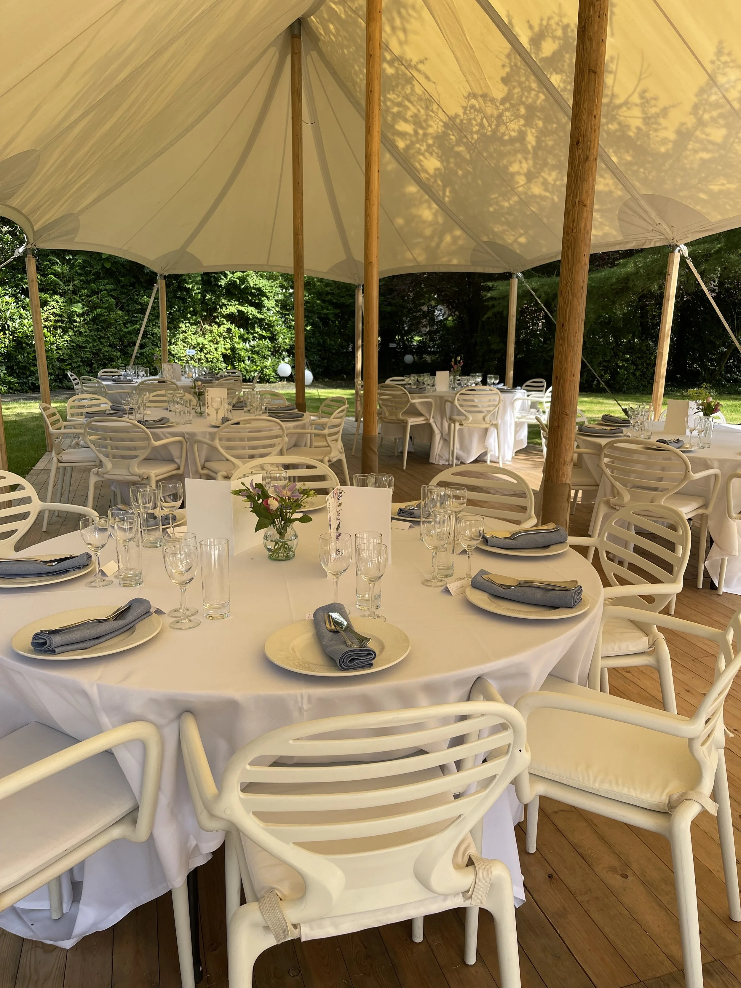 Zaal met ronde tafels en witte stoelen onder een grote witte tent, klaar voor een feest of bijeenkomst, met een bos bloemen als decoratie op tafel. #chefvandenberghe , chef van den berghe , private dining, private chef aan huis