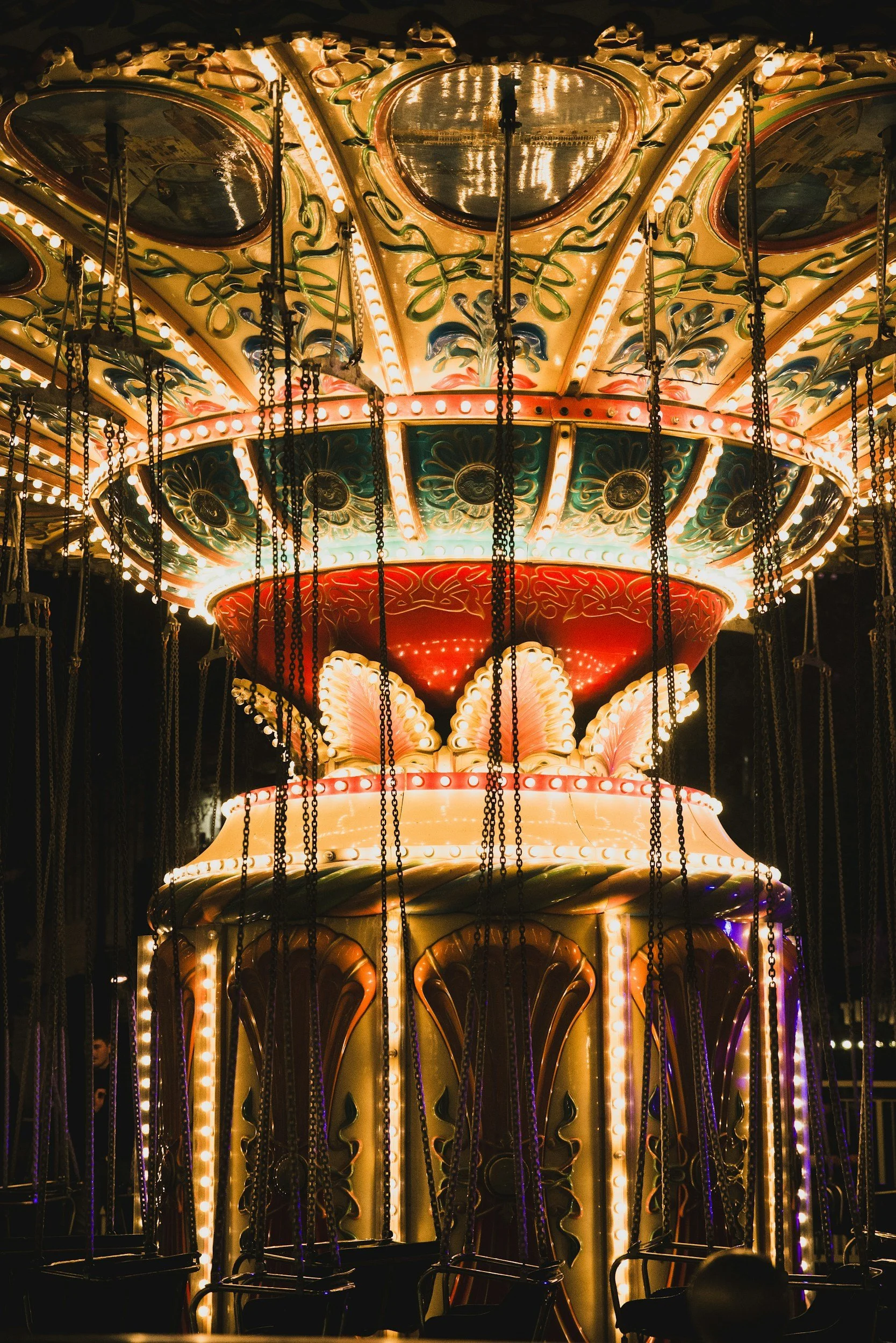 Close-up of a brightly lit vintage swing ride at night, showcasing elaborate decorative details and chains hanging from the top.