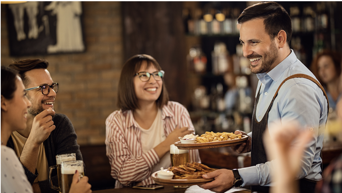 A smiling bartender serving food to happy friends in a cozy bar or pub.