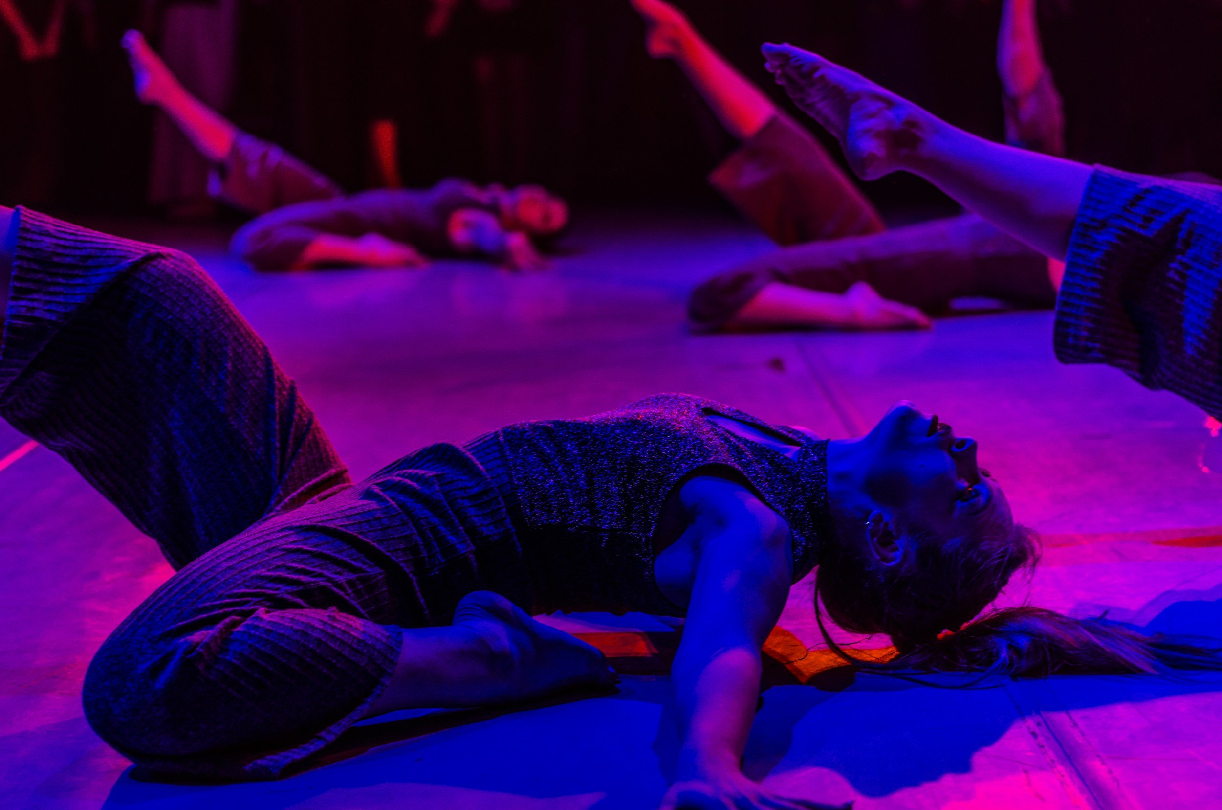 Group of people practicing yoga or stretching on a stage illuminated with purple and pink lighting.