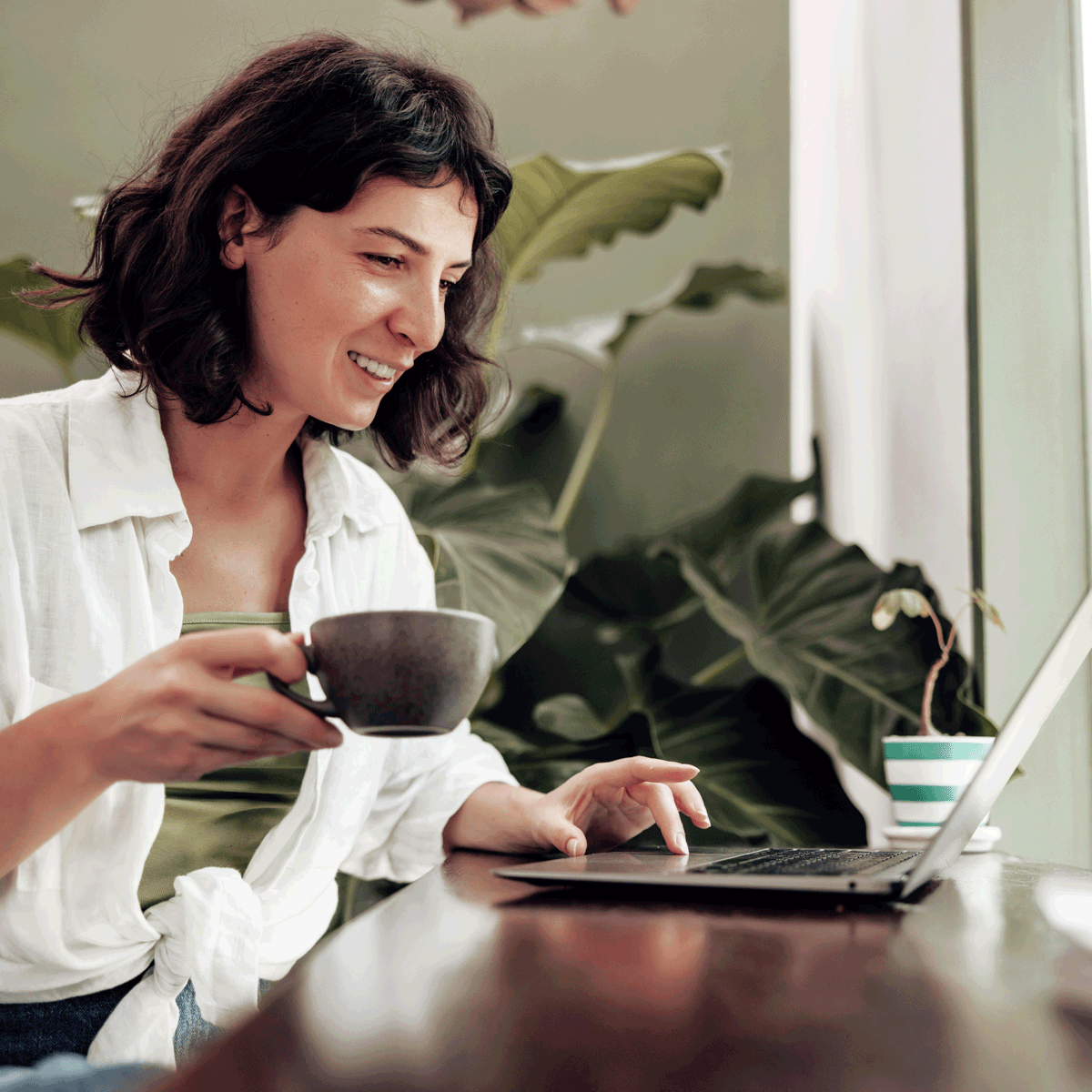 woman in her thirties having coffee and checking her finances on her laptop. She's happy that her pensions are supported.