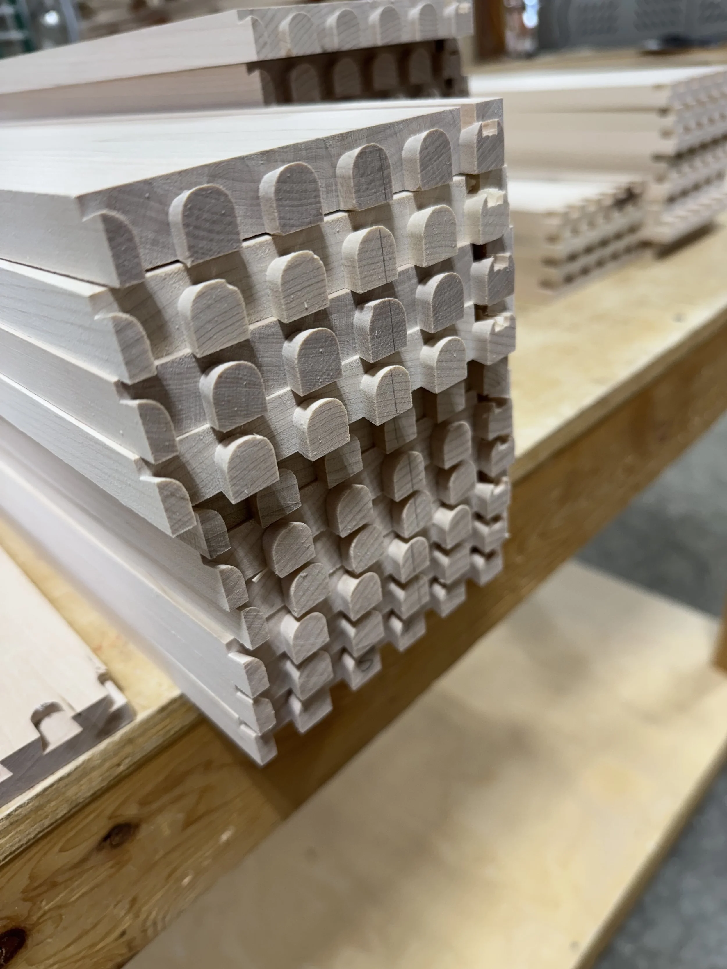 Stacked unfinished wood pieces with semi-circular notches, placed on a wooden workbench in a woodworking shop.