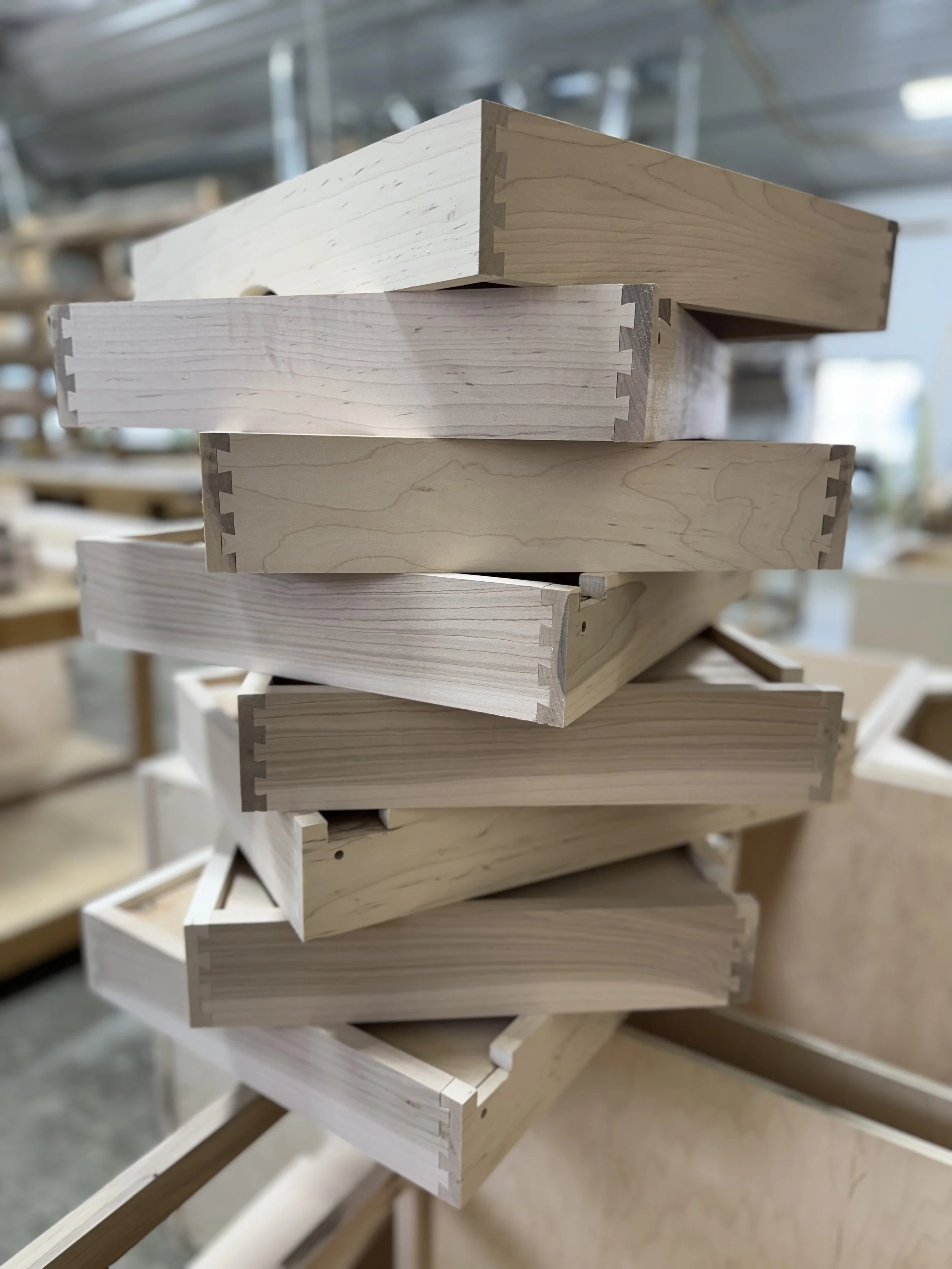 Stack of unfinished wooden drawer parts with dovetail joints in a woodworking shop.