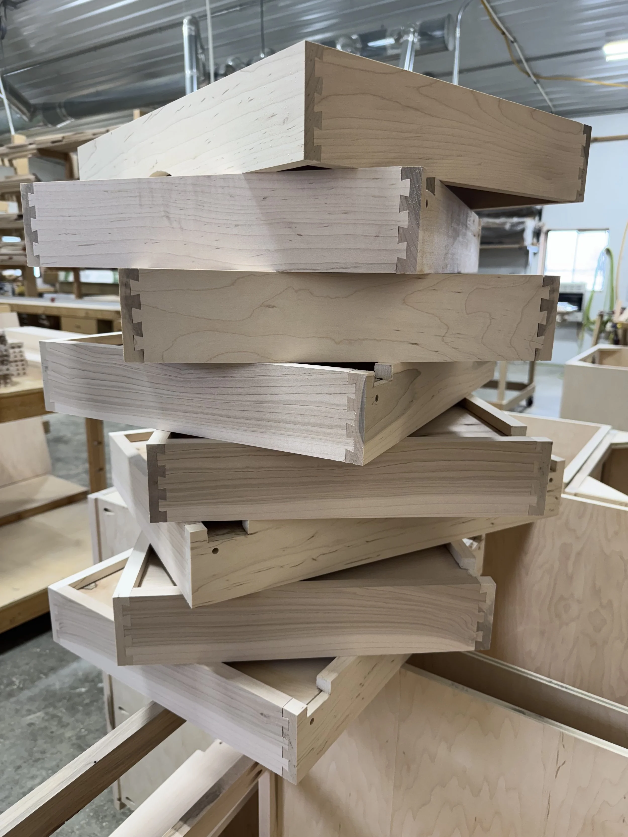 Stack of unfinished wood drawer parts in a woodworking shop.