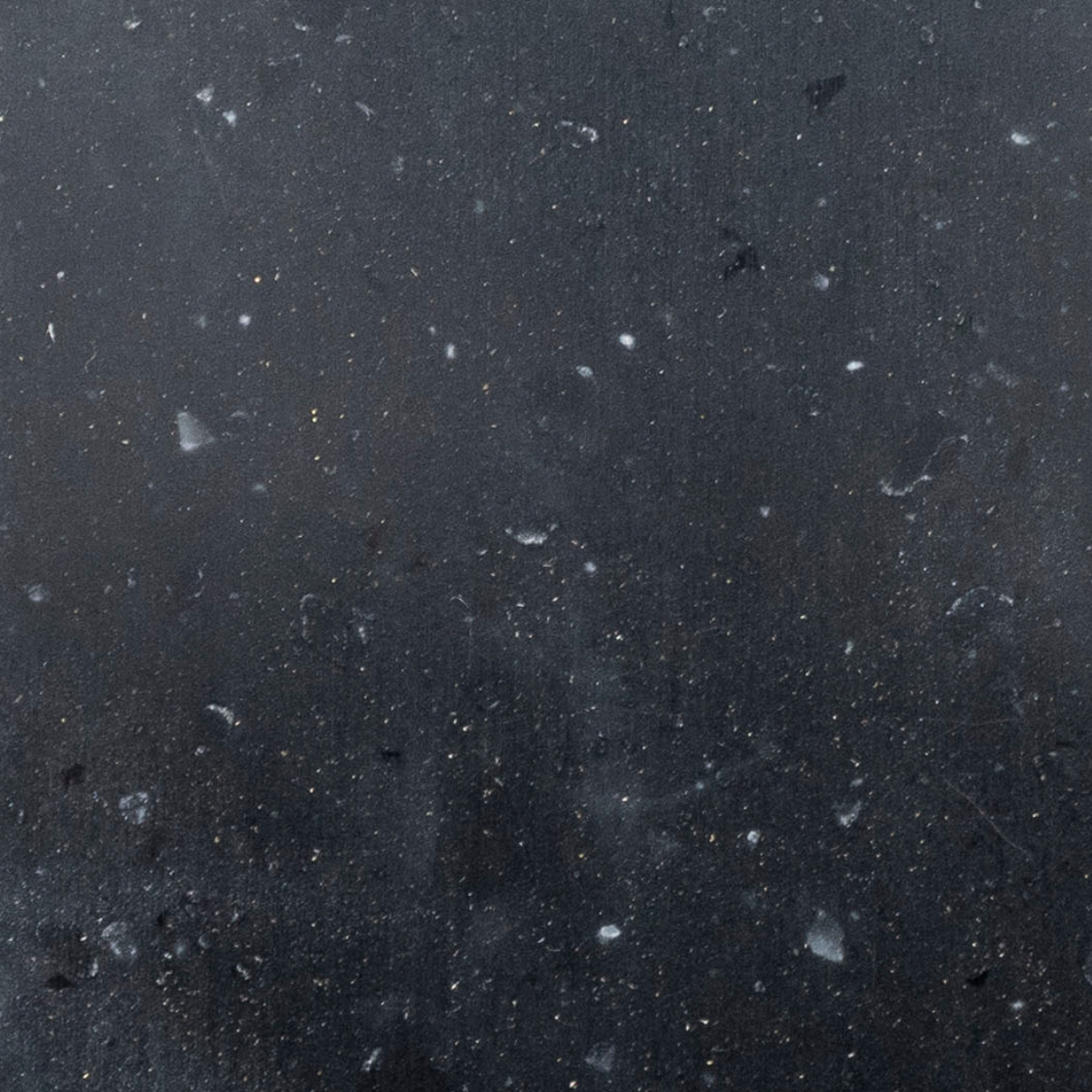 Close-up of a dark, textured countertop surface with small white specks and particles scattered throughout.