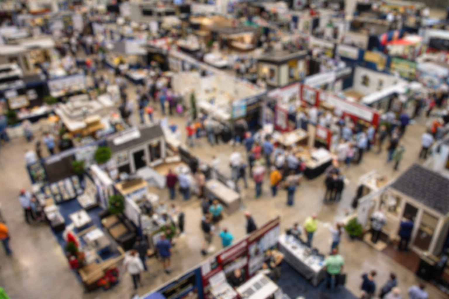 Blurred aerial view of a crowded indoor market with multiple stalls and many shoppers.