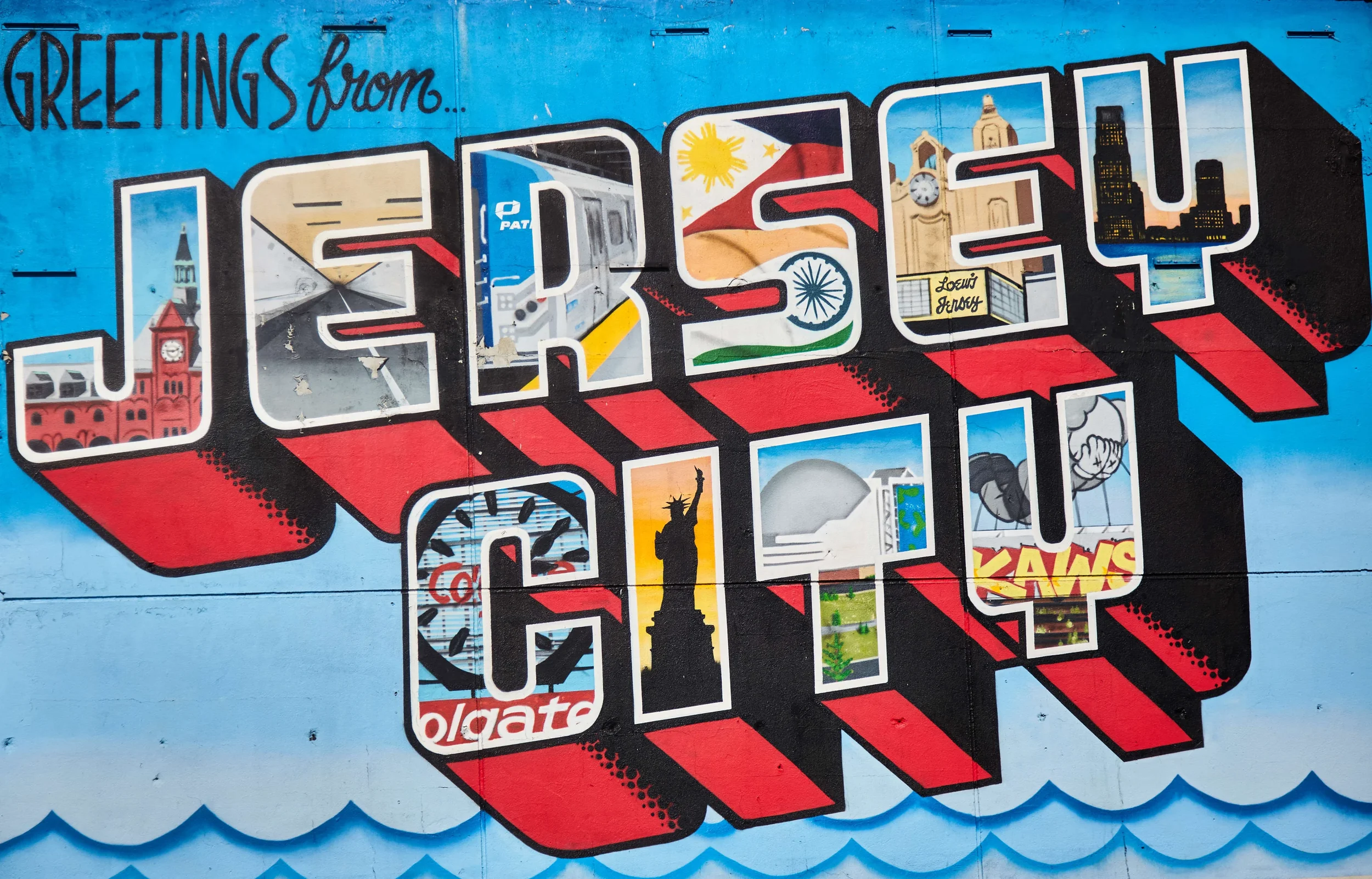 Colorful mural with the words 'Greetings from...' and 'Jersey' filled with iconic images of New Jersey landmarks and symbols, including the Statue of Liberty, rhythmic clock tower, city skyline, and diverse cultural references.