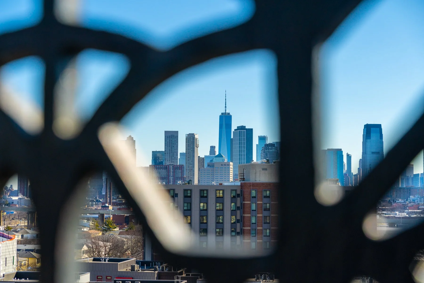 City skyline view of Manhattan, New York, with the One World Trade Center in the center, seen through a decorative black metal fence.