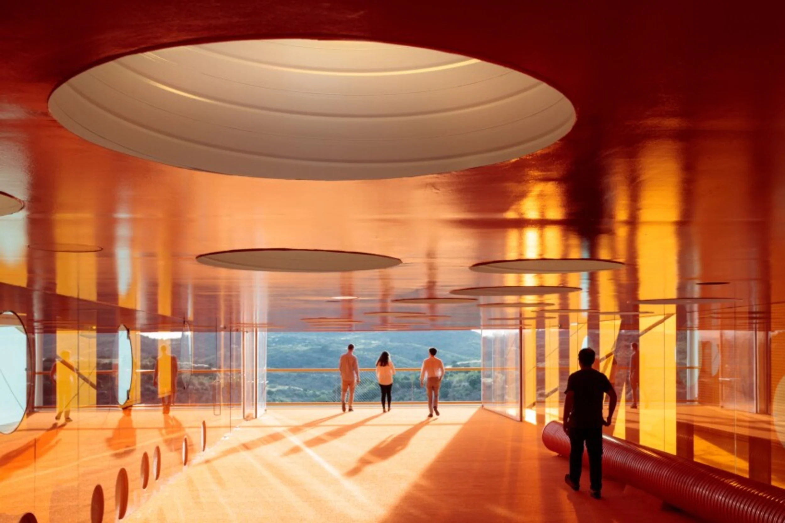 Vista de una estructura moderna con techo naranja y ventanas grandes, personas caminando y un paisaje natural al fondo.