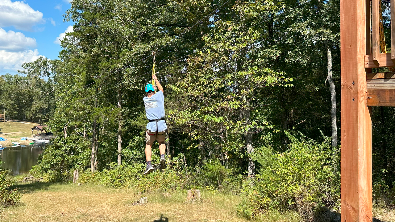 Person zip lining through a wooded area near a lake.