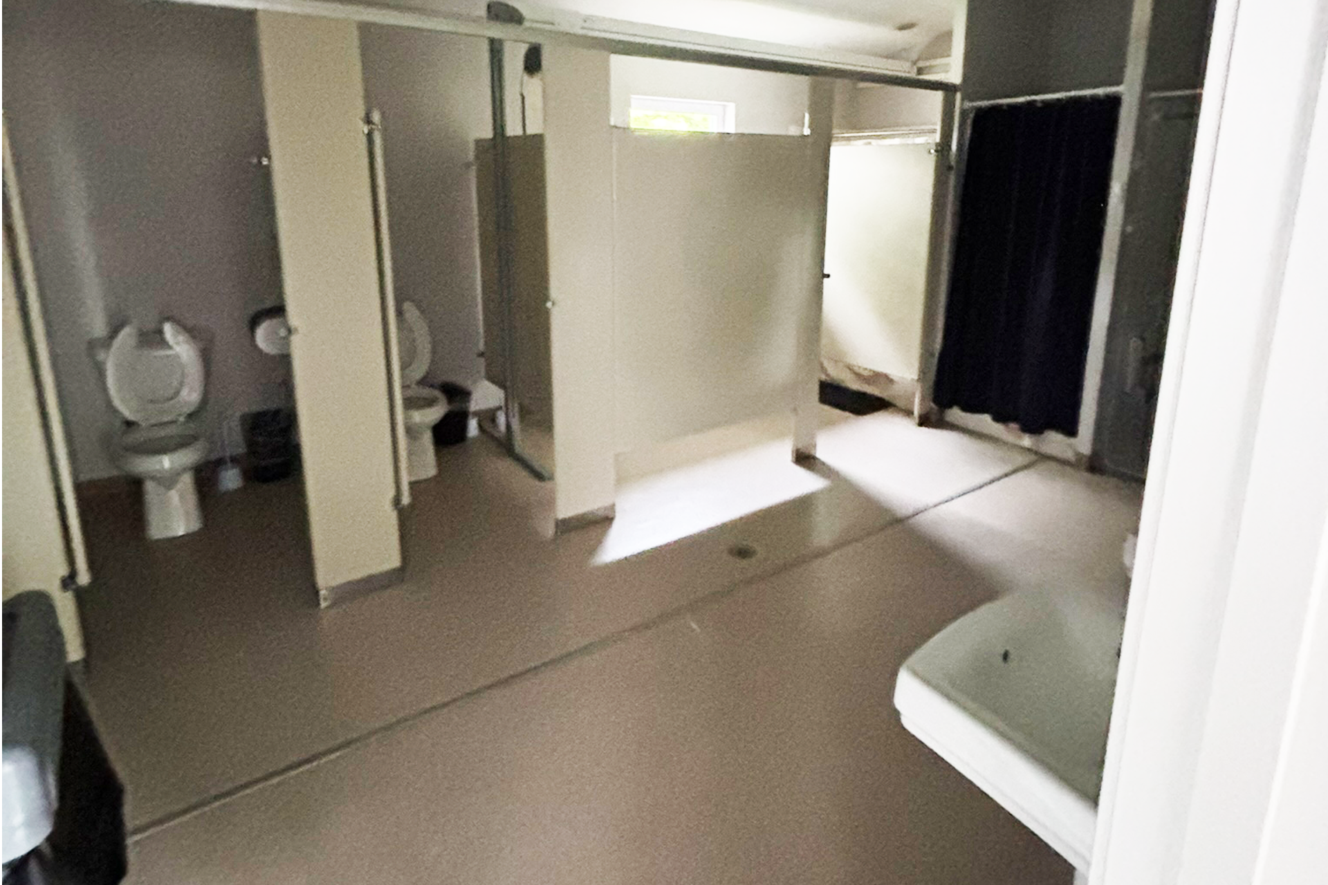 Public restroom with four toilets and a sink in a row, separated with partitions, and a black curtain covering an opening at the back.