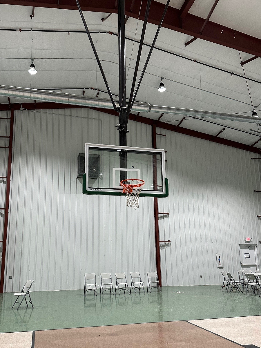 Indoor basketball hoop with a row of chairs on the floor and tables in the background.