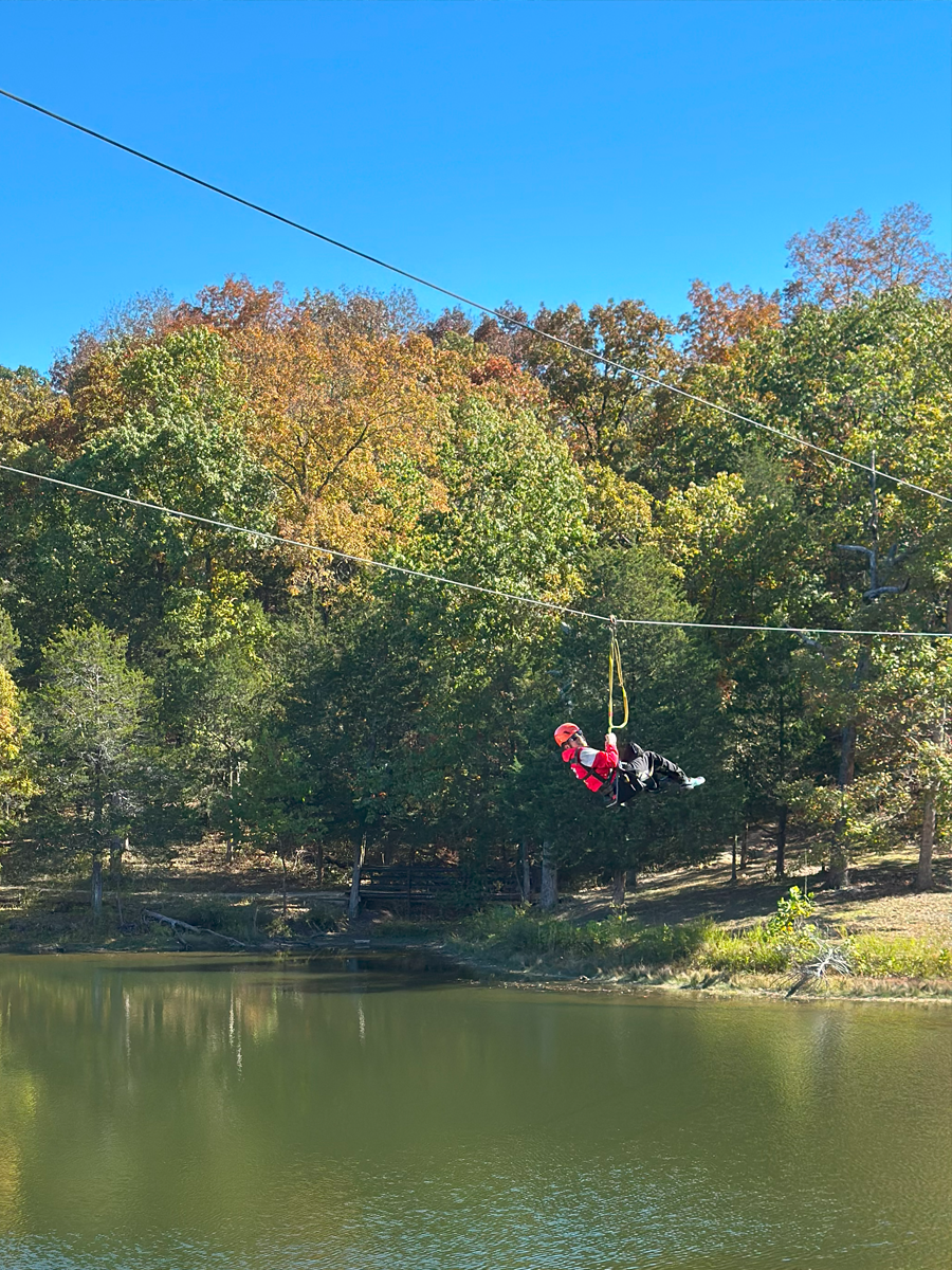 Person zip lining over a lake with trees in the background under a clear blue sky.