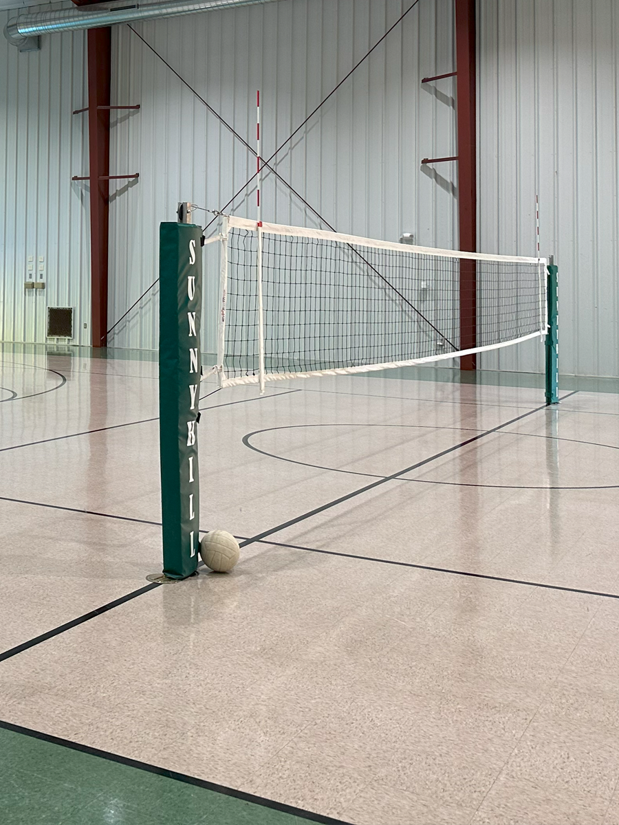 Indoor volleyball court with a volleyball leaning against a padded pole on the left side.