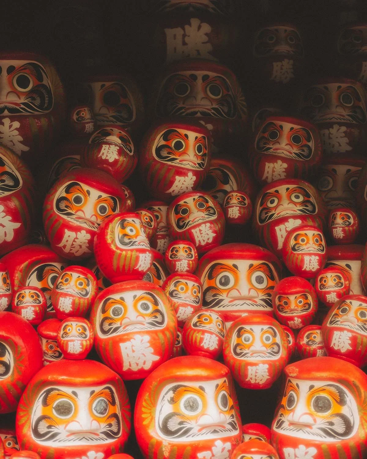 Milliers de poupées Daruma rouges symbolisant la chance et la persévérance empilées dans un temple bouddhiste au Japon. Photo de détail culturel par Dimitri Weber.