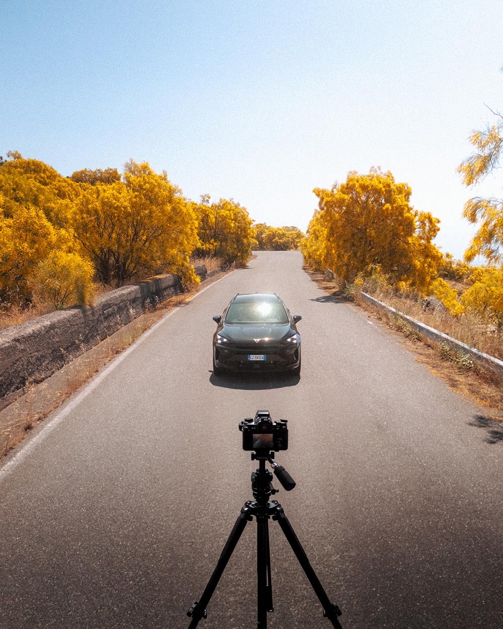 Behind the scenes d'un shooting voiture avec trépied et boîtier sur une route bordée d'arbres jaunes. Dimitri Weber, photographe automobile.