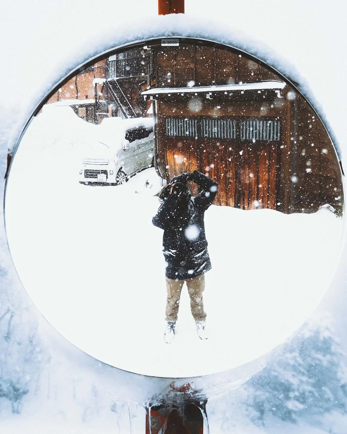 Autoportrait créatif du photographe Dimitri Weber capturé dans le reflet d'un miroir routier convexe sous une forte chute de neige. Ambiance hivernale immersive.