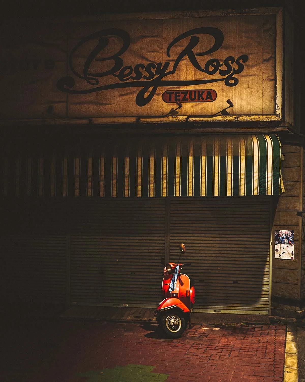 Nostalgie nocturne. Une devanture rétro et son scooter sous un éclairage urbain.